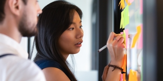 Jonge Aziatische vrouw schrijft met stift op bord vol met post-it notes